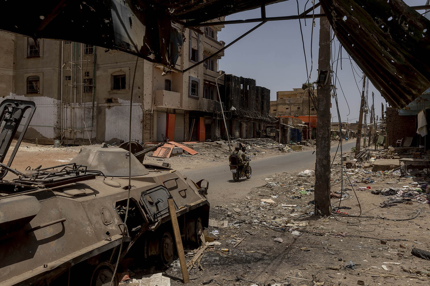 SAF soldiers ride a motorcycle past a destroyed armoured people carrier in Al-Shaabi market