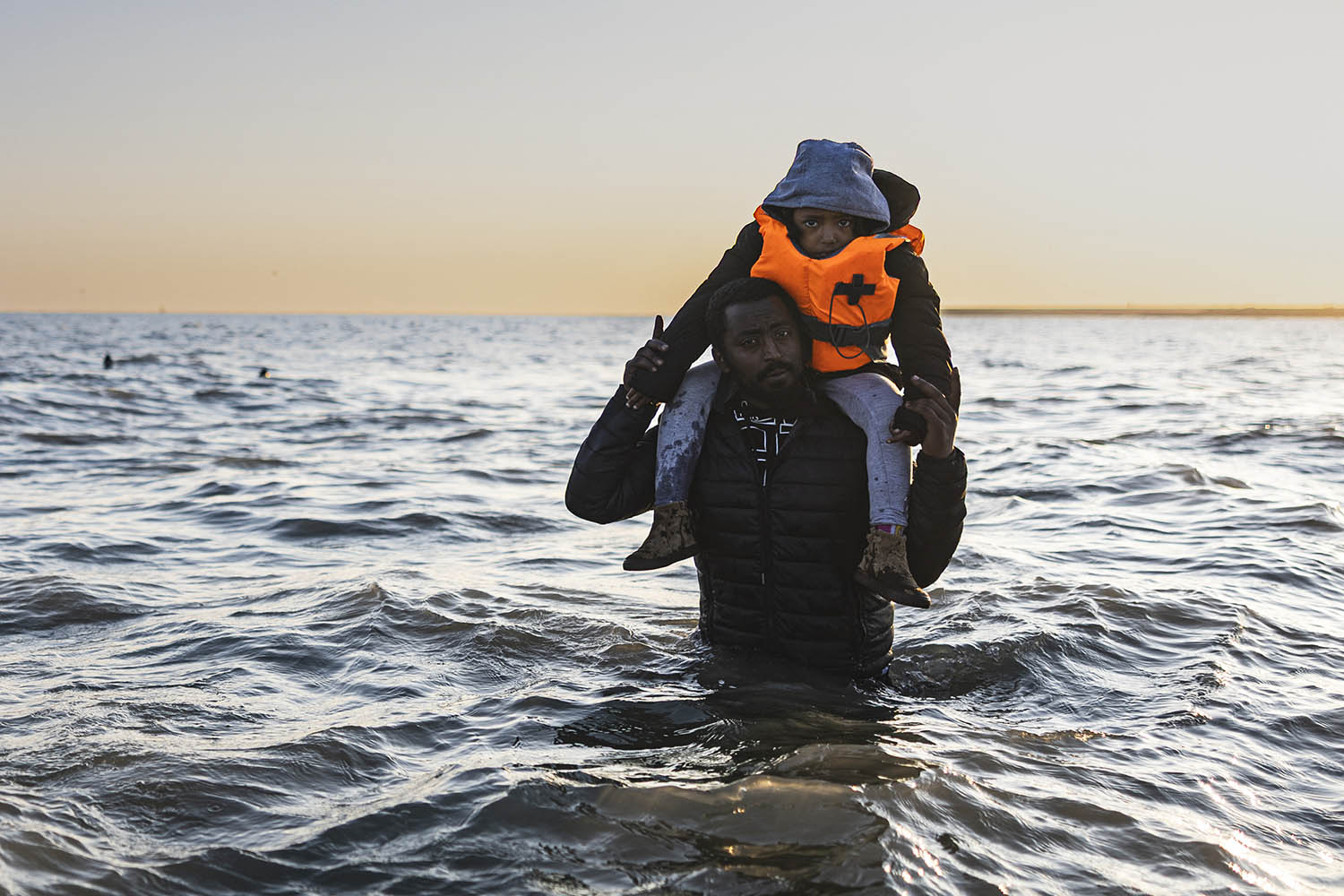 A father carries his child into the English Channel at sunrise from the beach at Gravelines in northern France