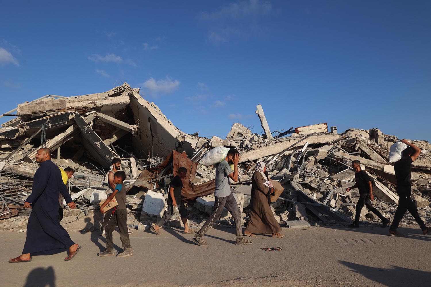 People, some carrying aid parcels, walk along the Salah al-Din road near the Nusseirat refugee camp in the central Gaza Strip.